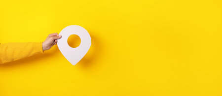 3D location symbol in hand over yellow background, panoramic imageの写真素材
