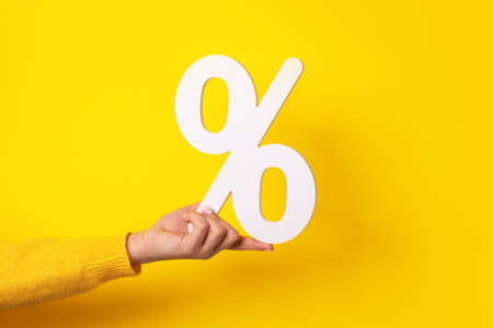 hand holding percentage sign over yellow backgroundの写真素材