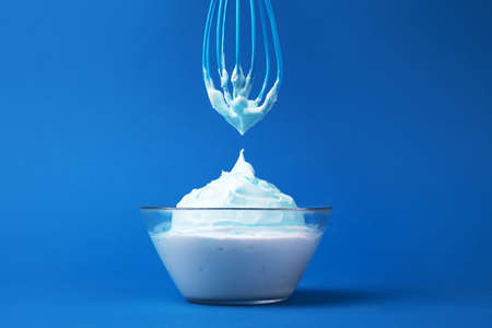 whipped cream with whisk over blue background