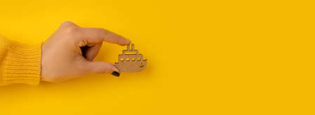 wooden ship in hand over yellow background, travel or summer vacation concept, panoramic mock-upの写真素材
