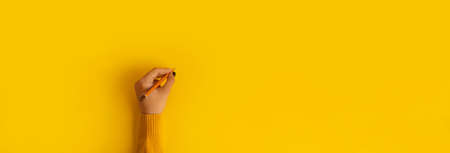 pencil in hand over yellow background, panoramic mock-upの写真素材