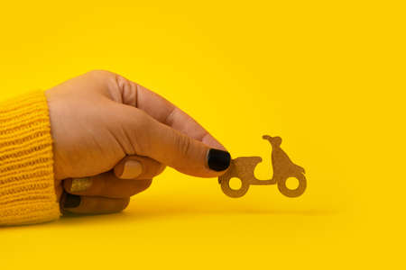 Fast and free delivery by scooter, wooden scooter in hand over yellow backgroundの写真素材