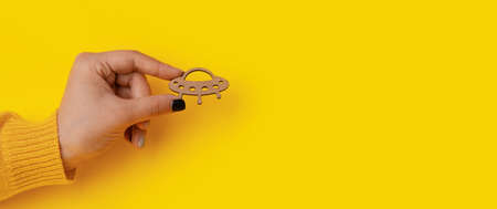wooden symbol UFO in hand over yellow background, panoramic mock-upの写真素材
