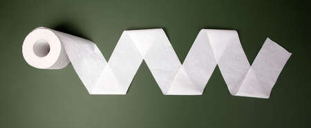A single roll of toilet paper unrolled over green background, panoramic image