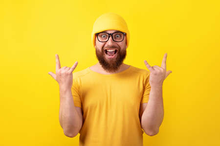 funny man makes rock n roll gesture over yellow background