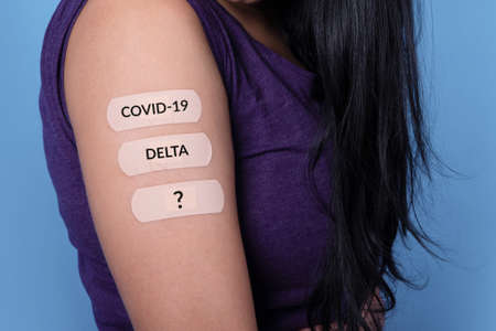woman showing many plasters on shoulder with inscription covid-19, delta, after coronavirus vaccine, new stamps and mutation conceptの写真素材