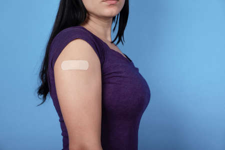 woman over blue background showing plaster on shoulder after coronavirus vaccine, immunization, prevention concept.の写真素材