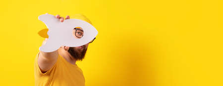 man holding rocket over yellow background, guy with successful startup, panoramic layoutの写真素材
