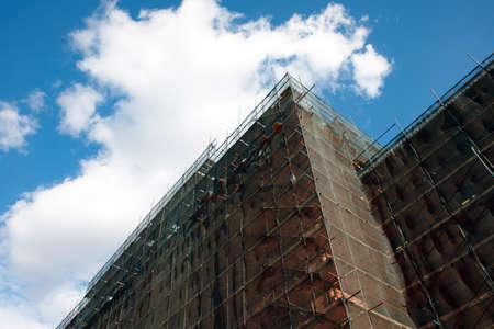 Building facade renovation over blue sky, old house reconstruction, repair. Scaffold in front of...