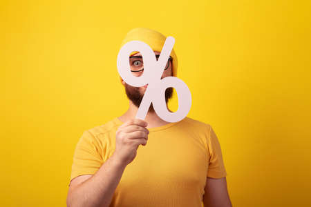 man holding 3D white percentage sign over yellow background, big sales conceptの写真素材
