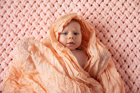 newborn baby looking into camera in a pink suit on a knitted plaid