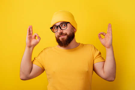 bearded man in glasses showing ok gesture over yellow backgroundの写真素材