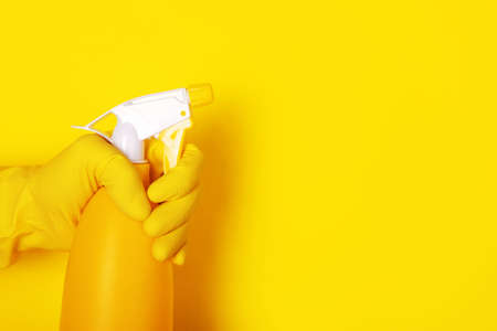 hand in a glove holding a spray bottle over yellow backgroundの写真素材