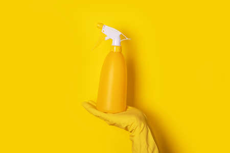 hand in a glove holding a spray bottle over yellow background, cleanliness conceptの写真素材