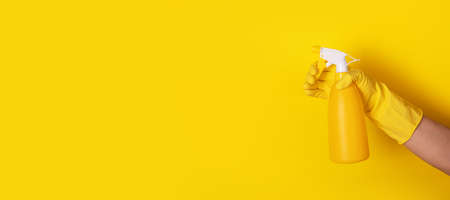 hand in a glove holding a spray bottle over yellow background, cleanliness concept, panoramic layoutの写真素材