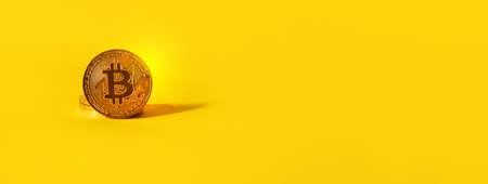 A bitcoin resting on a pile of bitcoins on a yellow background, panoramic layout