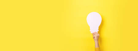 hand holding light bulb over yellow background, panoramic layoutの写真素材
