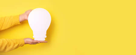 hands holding light bulb over yellow background, panoramic layout