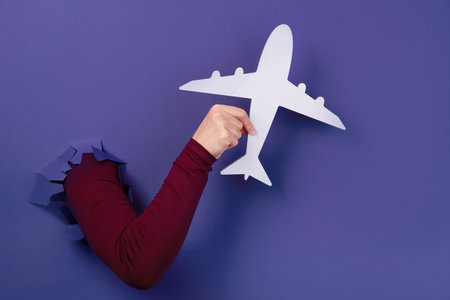 hand holding white airplane over purple background, air travel conceptの写真素材