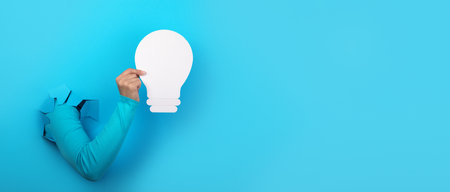 hand holding light bulb over blue background, panoramic layout