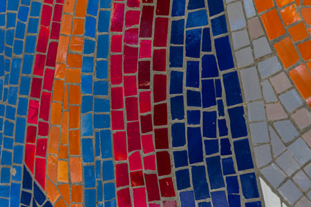 Close-up view of vibrant mosaic tiles in red, orange, blue, and gray arranged in flowing patterns, perfect for artistic and design projects.の写真素材