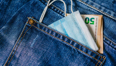 Medical face mask and money in jeans back pocket background. Concept for the new normal or new lifestyle after COVID-19 Coronavirus pandemic.の写真素材