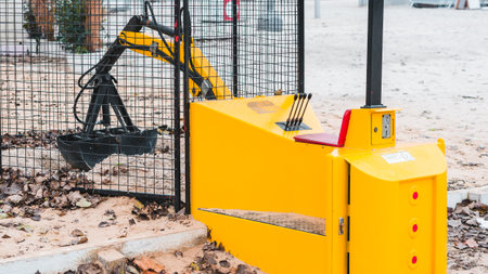 small yellow excavator for money picks up sand behind the fence