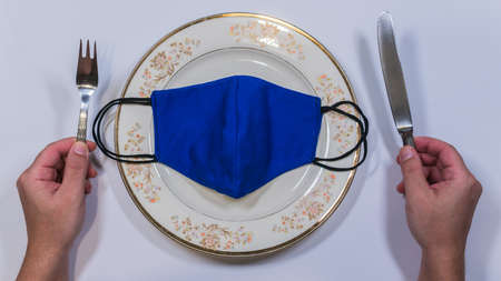 Medical Mask on an Empty Plate with Fork And Knife on a White backgroundの写真素材