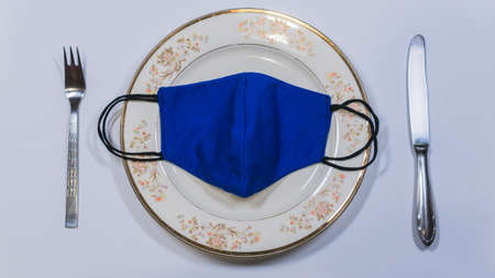 Medical Mask on an Empty Plate with Fork And Knife on a White backgroundの写真素材