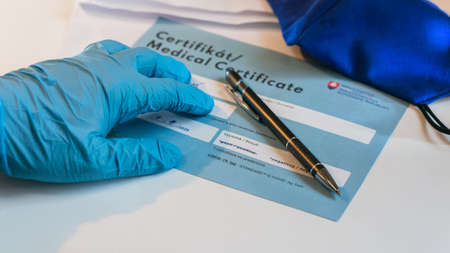 Bratislava, Slovak Republic - 09.02.2021: laboratory assistant analyzes negative PCR certificate of covid-19 in on white table with pen and mask, conceptual image, Slovakiaのeditorial素材