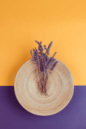 Bunch of smelling lavander flower on a wooden round plate on orange and lavander colored background top view.の写真素材