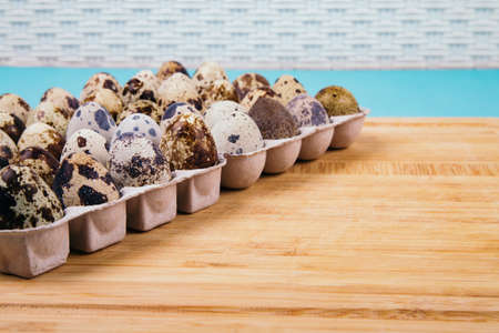 Quail eggs in paper box on wooden board on blue background, side view.の写真素材