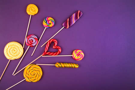 Many colorful lollipop candys arranged in heap with heart shaped candy in the center on violet background. Flat lay concept.の写真素材