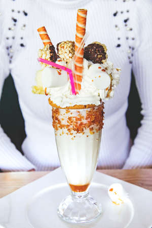 Woman cropped body weared in white sweater and glass of caramel milk shake coctail covered with chocolate, whipping cream, waffles and straw. Cropped frame.の写真素材