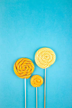 Three yellow  colorful lollipop candys arranged together on blue background. Flat lay concept.の写真素材