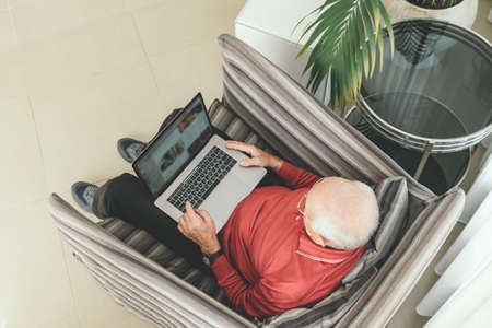 Old retired pensioner in glasses with white hair sits infront of the computer and serf web-sites at...