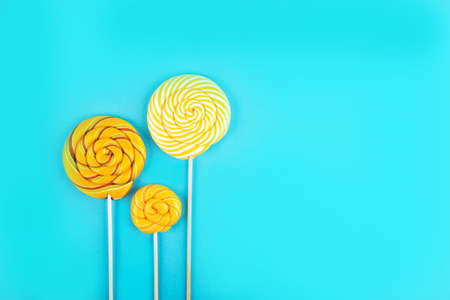 Three yellow  colorful lollipop candys arranged together on blue background. Flat lay concept.