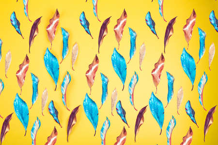 Vibrant vivid red, blue and yellow colored acrylic painted leaves on yelow background texture. Flat...
