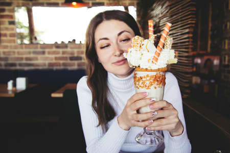 Caucasian happy brunette woman with stylish french manicure holds glass of caramel milk shake...