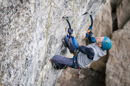Drytooling man holding special equipment for climbing in blue helmet climbs an overhanging rock.