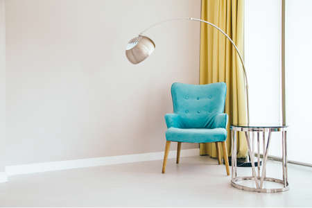 Conceptual light  interior of living room with blue armchair, metallic standing lamp,  glass round coffee table ,large window and yellow curtain. Concept of minimalizm.の写真素材