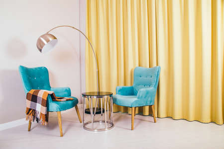 Conceptual light  interior of living room with two blue armchairs and brown blanket, round glass coffee table, metallic  standing lamp and yellow curtains.の写真素材
