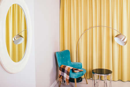 Conceptual light  interior of living room with blue armchair and brown blanket, round glass coffee table, metallic  standing lamp, yellow curtains and oval mirror on the white wall.の写真素材