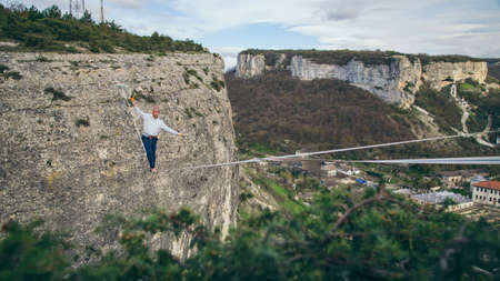 Man walking on high line and attempt to stand up and make step above mountains. High line contest.の写真素材