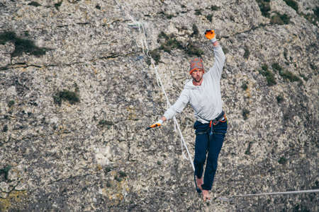 Man walking on high line and attempt to stand up and make step above mountains. High line contest.