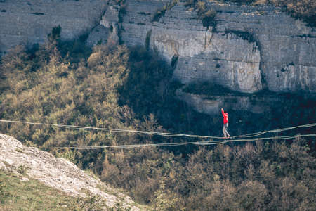Man in red clothing walking along high line above mountains landscape. High line contest.の写真素材