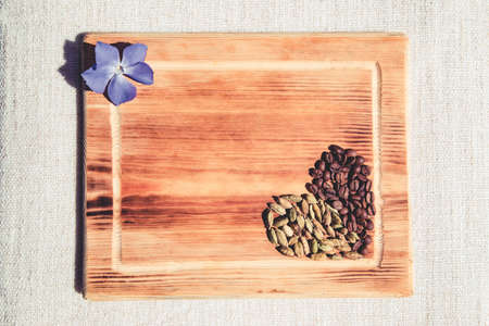 Composition of coffee and cardamom grains in heart shape and violet flower on wooden board. Flat lay...