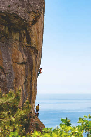 Group of sportsman (woman and two man) climbing rock mountain high route against blue sea and sky...