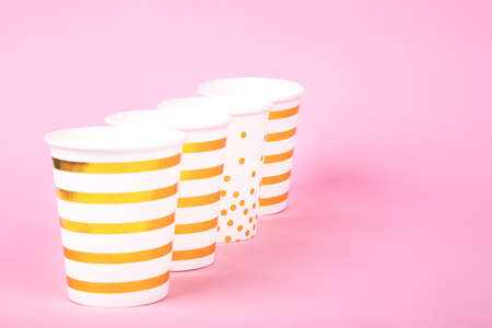 Party style white paper disposable cups with golden stripes, spots and stars prints on pink background. Flat lay style.の写真素材