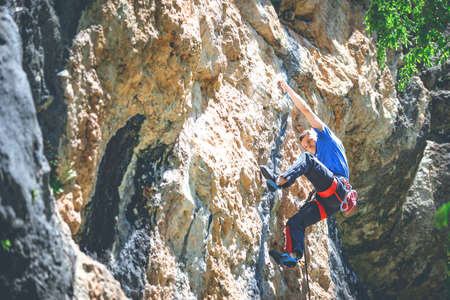 Athletic man climbs a rock in the forest with rope. Sport climbing, lead.